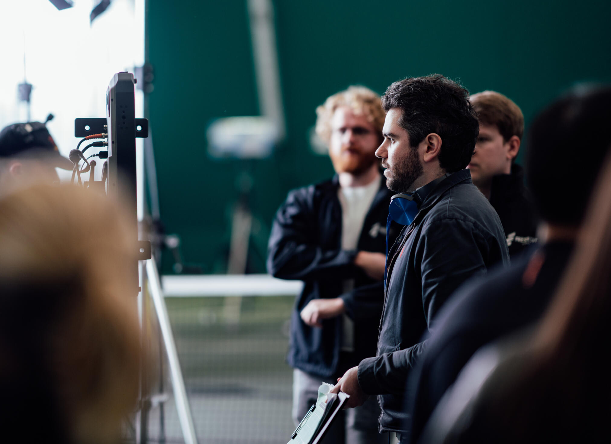 A director and the support team looking at a monitor on a sports film set.