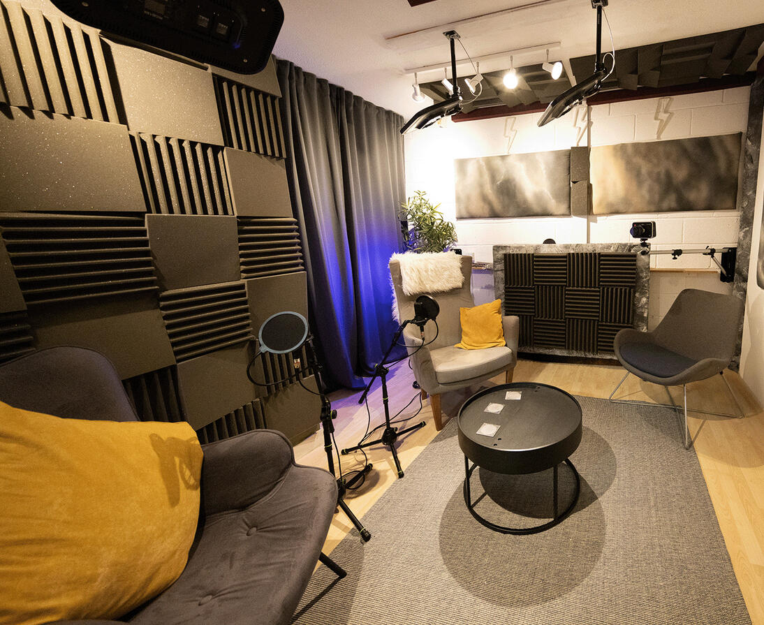 A podcast studio, decorated with comfortable chairs and sound insulation with high end microphones.